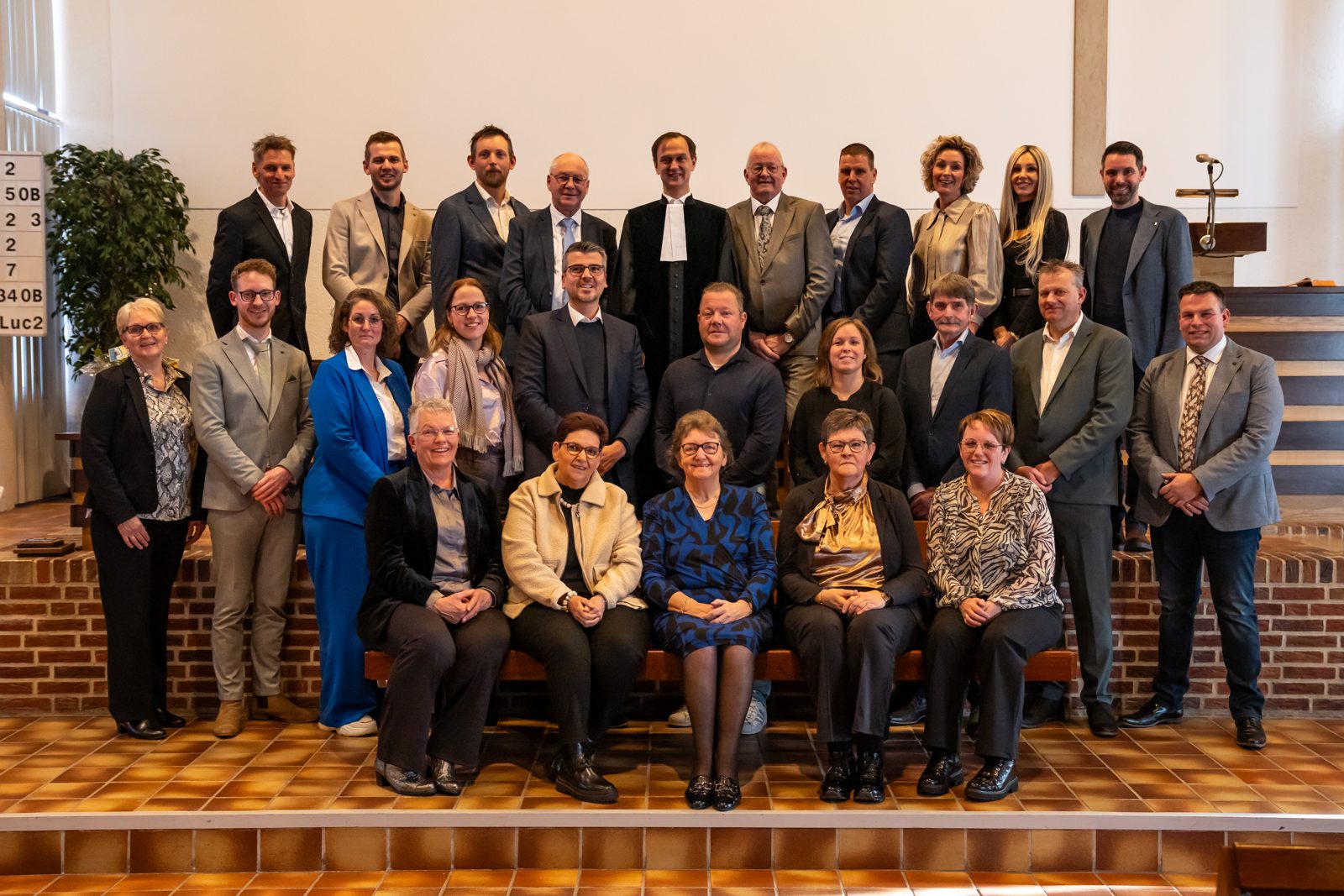 Groepsfoto van de kerkenraad van de Hervormde Gemeente Westerhaar in de kerkzaal, met de predikant in toga in het midden.