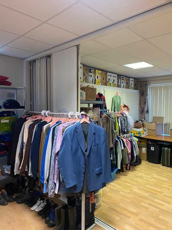 Kledingrek met blouses en vesten, met daarachter vakkenkasten vol opgevouwen kleding.