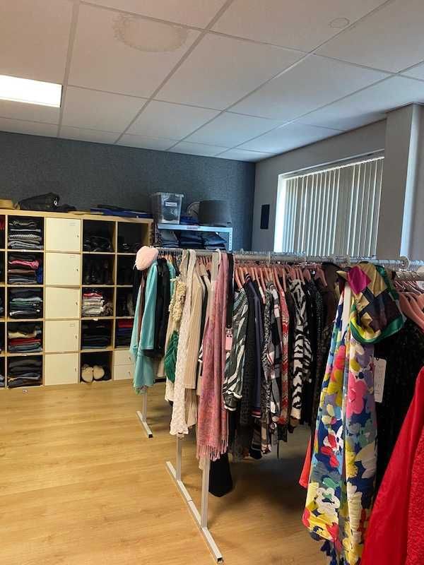 Vakkenkasten met kinderschoenen, kleding en speelgoed langs de wand.