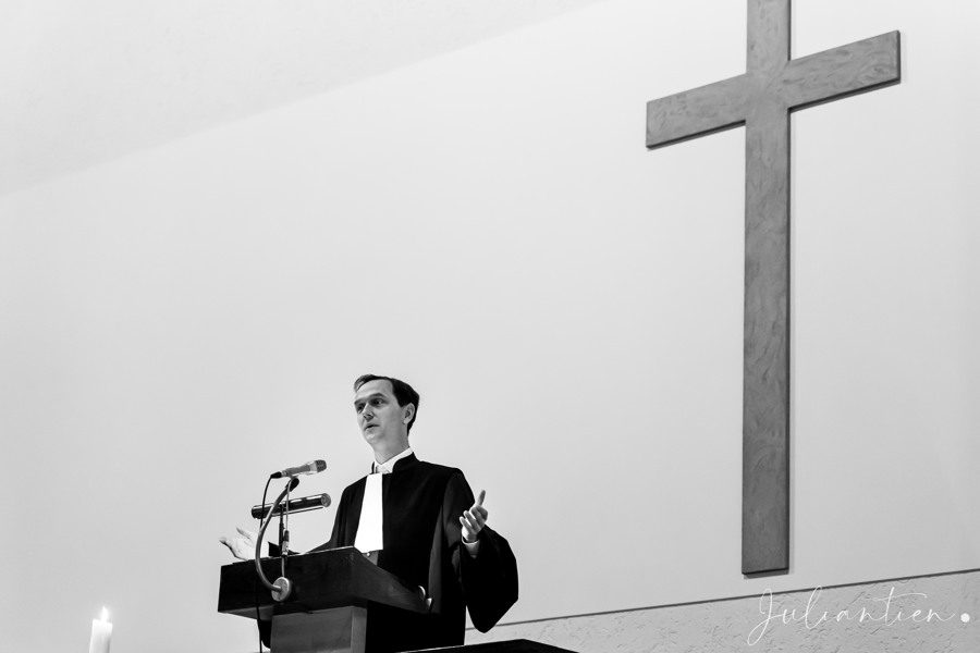 De predikant achter de kansel tijdens een dienst, met het kruis aan de muur erachter.